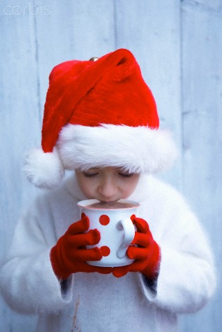 Boy in Father Christmas hat drinking mug of hot chocolate
